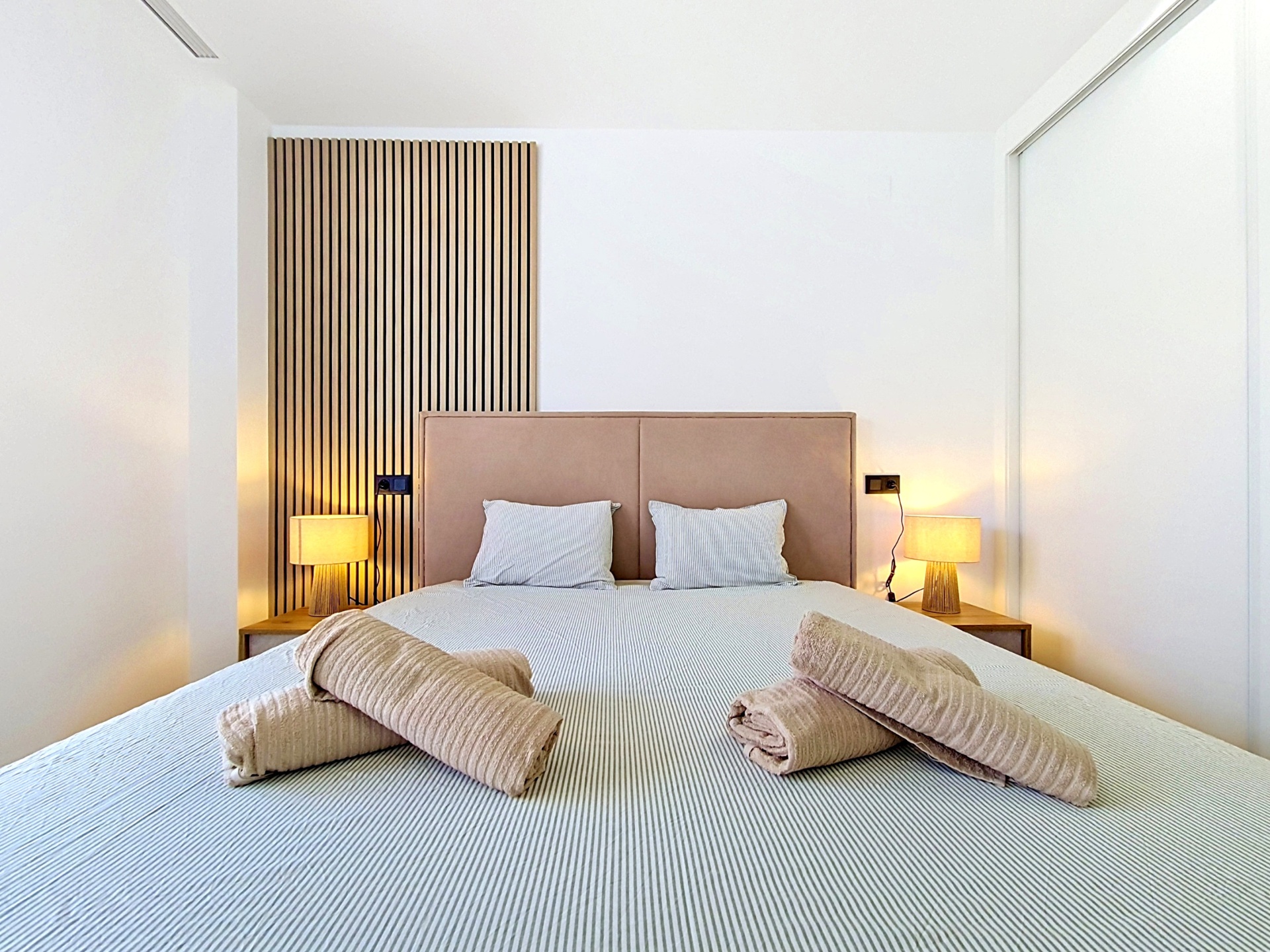 Main bedroom straight-on view with bedside tables and slatted wall