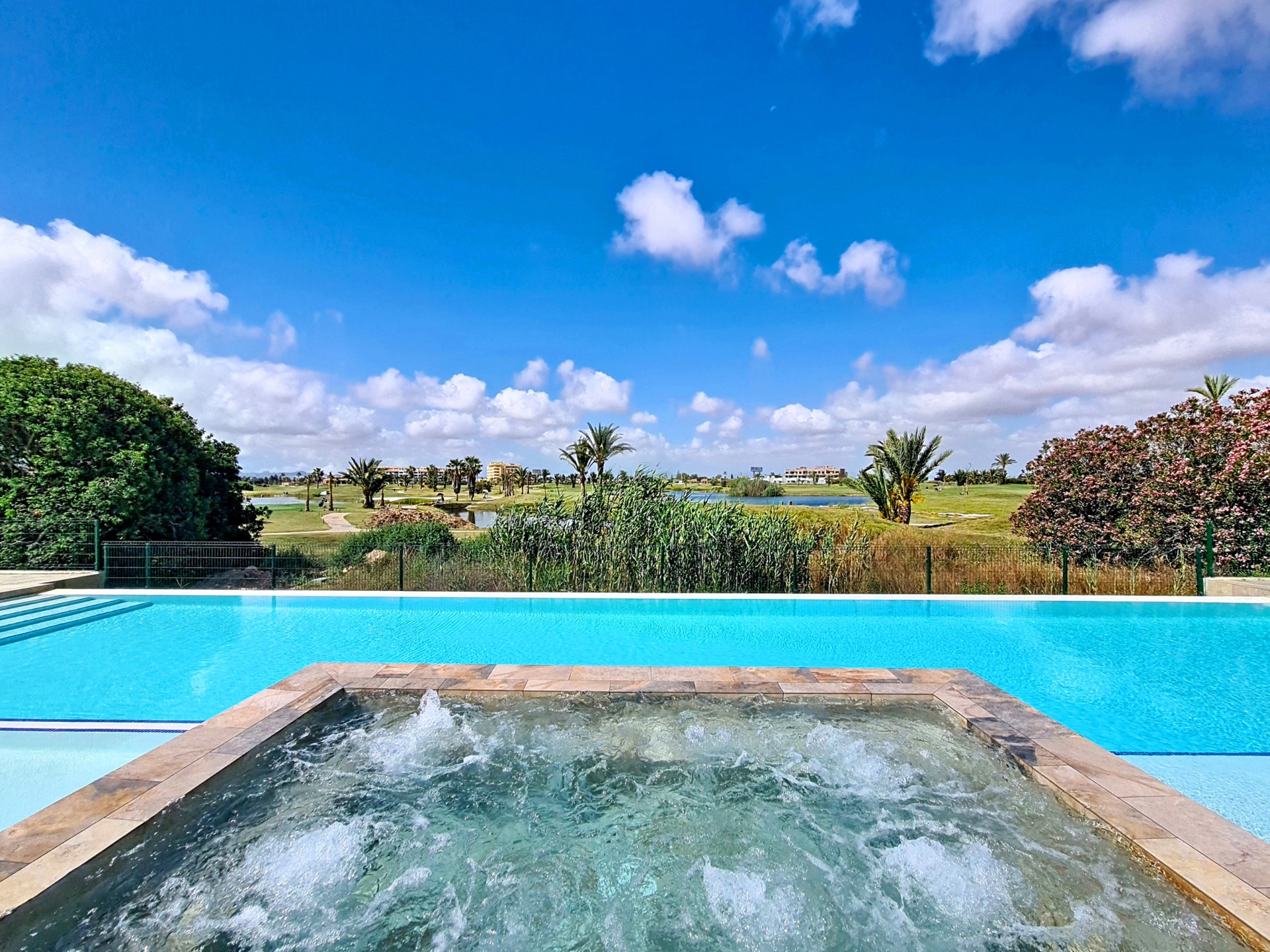 Infinity-style communal pool with jacuzzi and golf course backdrop